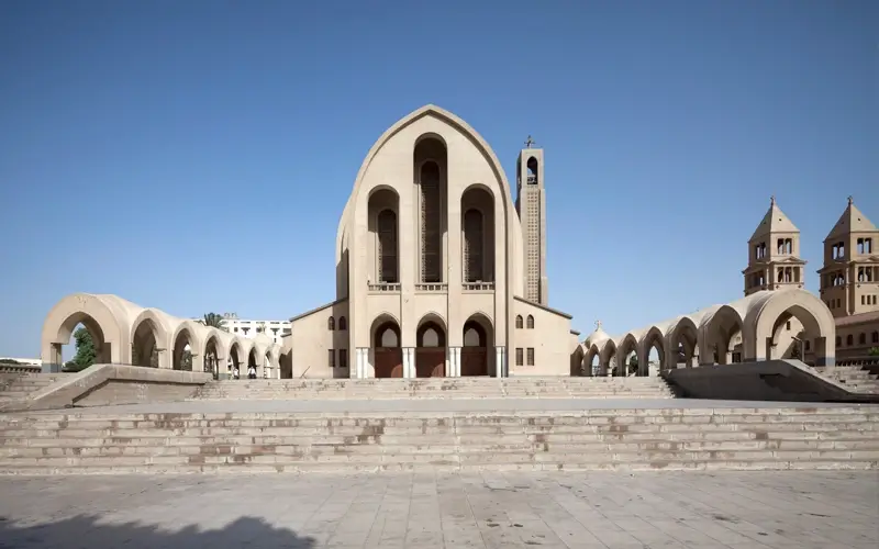 Exterior architecture of the Coptic Orthodox Church in Egypt featuring traditional beige stone and tall central arches.