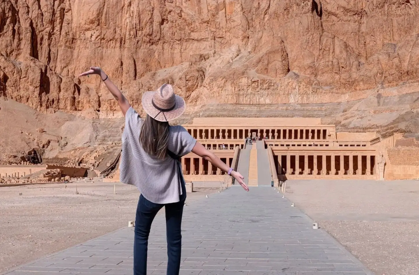 Female traveler with arms wide open standing in front of the Mortuary Temple of Hatshepsut during a trip to Egypt in October.