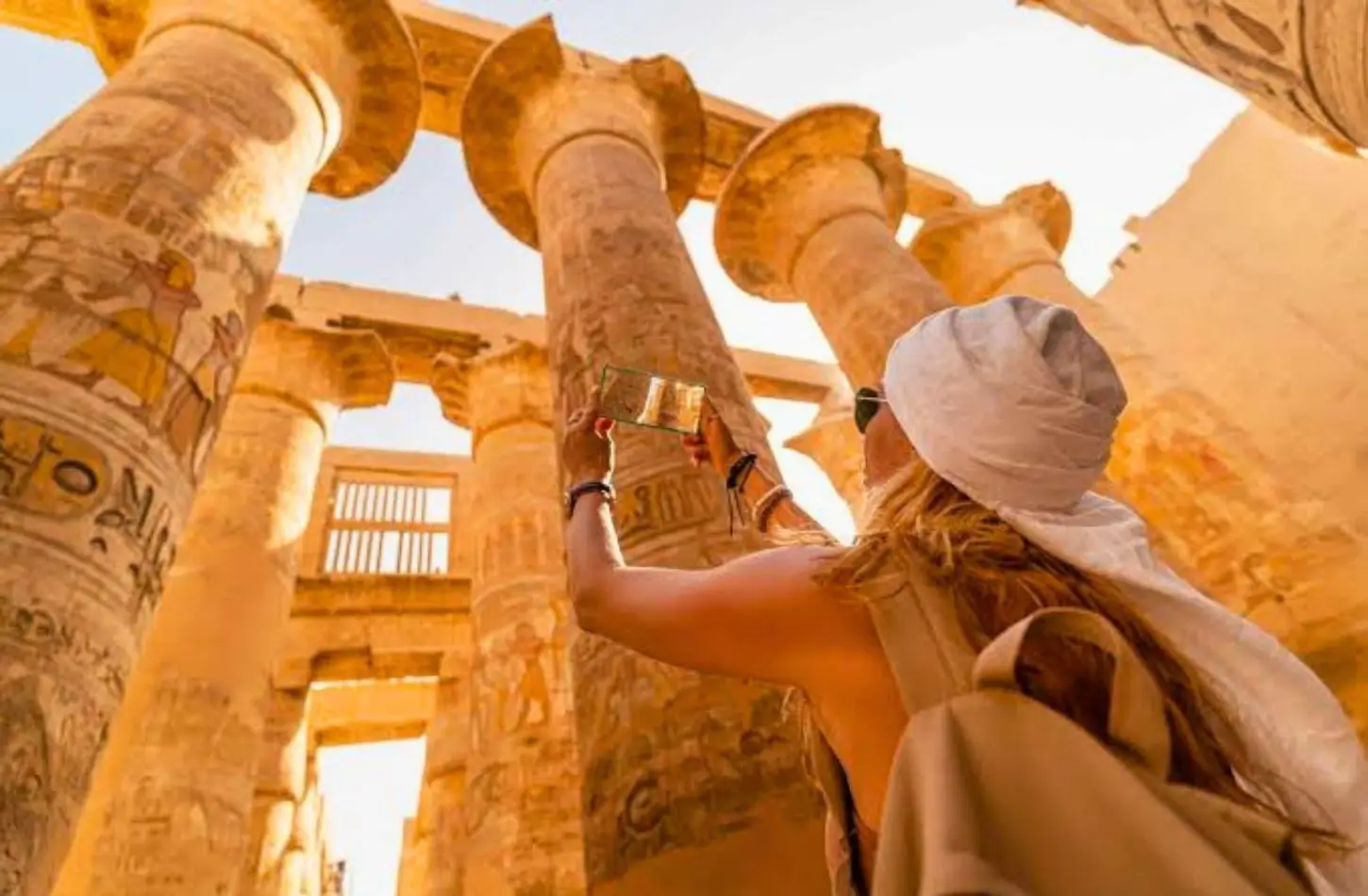 Woman taking a photo of ancient hieroglyphics on giant temple pillars while exploring Egypt in October.
